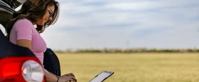 Woman sat in the boot of her car looking at a laptop