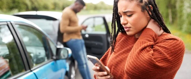 Young woman looking at phone after car accident with another driver