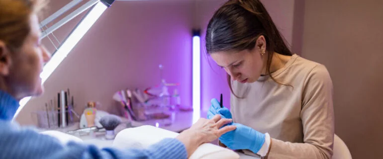Adult woman in blue sweater getting her gel nails done by young female nail technician