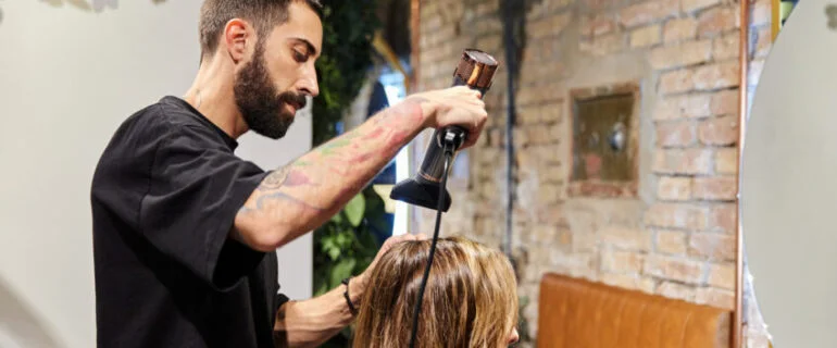 Side view of a bearded hairdresser drying a woman's hair with a blow dryer in a salon