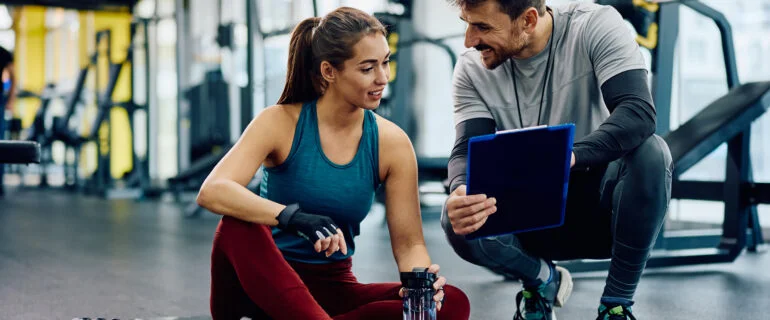 A personal trainer talks his female client through a training schedule in a gym