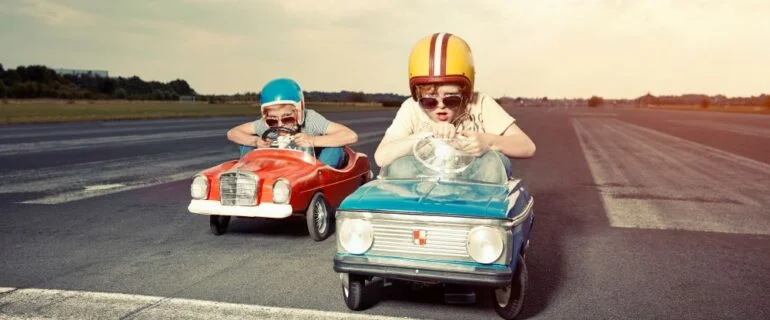 Two boys in pedal cars wearing helmets crossing finishing line on race track