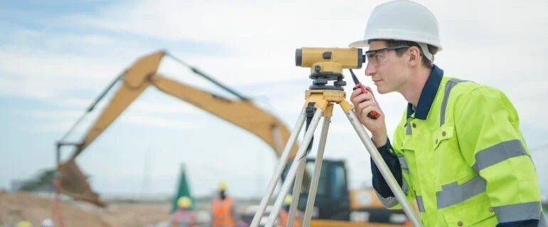 Male engineer working with survey equipment on construction site and worker background.Surveyor making contour plans is a graphical representation of the lay of the land startup construction work.