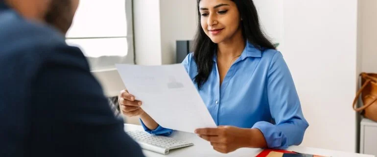 Professional Indian female recruiter manager reading candidate’s resume while doing a job interview in a modern office. Recruitment human resources employment hiring concept.