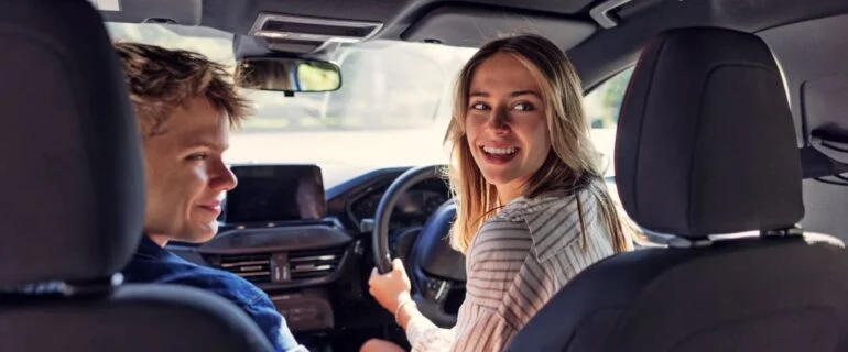Young female is driving a car with a young male companion in the passenger seat