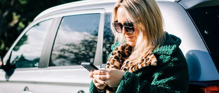 Woman leaning against car checking mobile phone