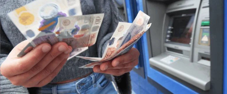 Young woman wearing jeans holds notes she has just withdrawn from a cash machine