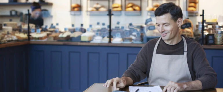 Business owner using calculator at a table in the small bakery or cafe which he runs