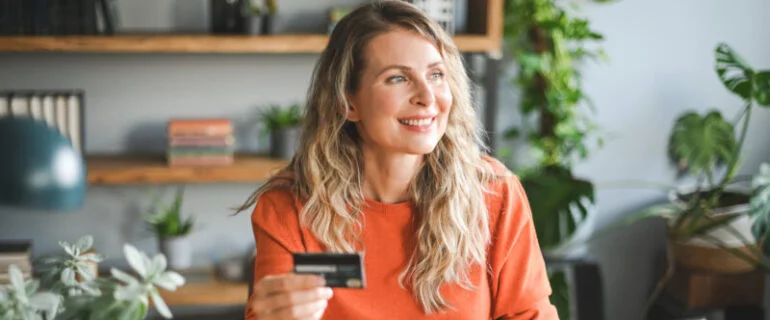 Woman working at home and holding up a credit card