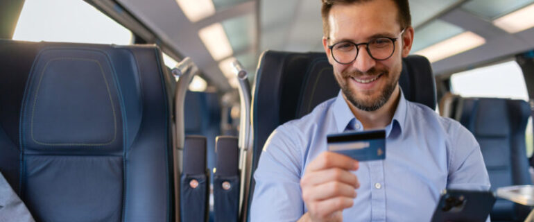 A happy man on the train uses his mobile phone to shop online by entering credit card information.
