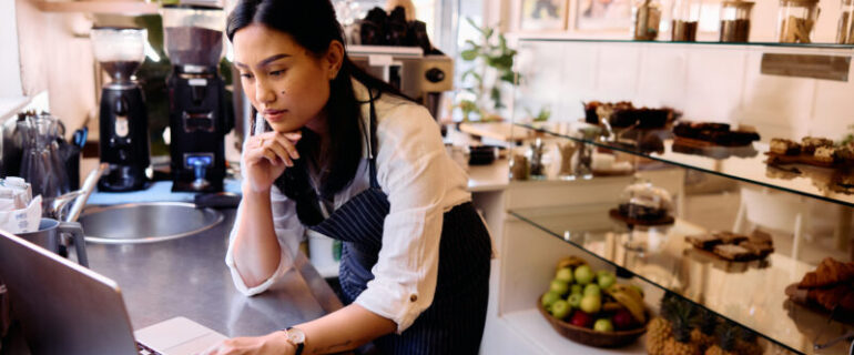 Woman in her 30s concentrating on computer in artisanal cafe, with hand on chin